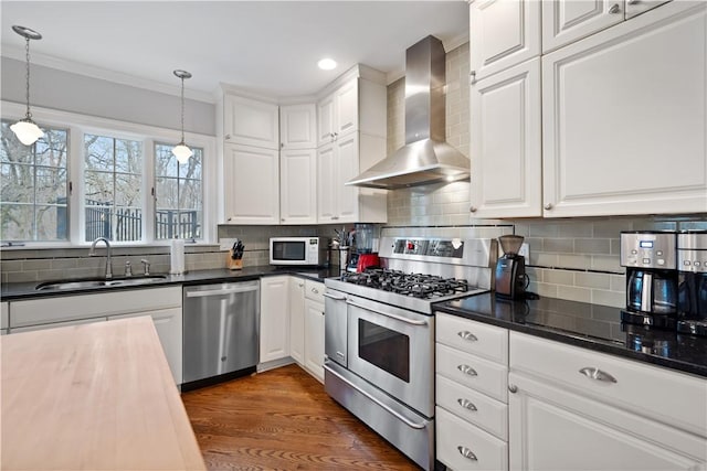 kitchen featuring stainless steel appliances, a sink, wall chimney exhaust hood, white cabinetry, and tasteful backsplash