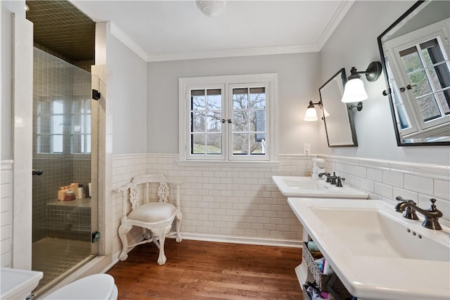 bathroom with tile walls, a shower stall, crown molding, wood finished floors, and a wainscoted wall