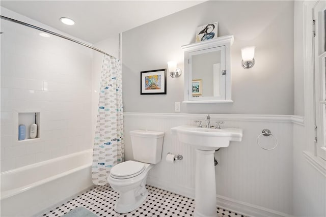 bathroom featuring toilet, a wainscoted wall, shower / tub combo, a sink, and tile patterned floors
