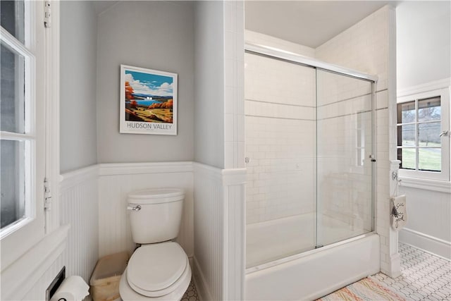 bathroom featuring wainscoting, toilet, bath / shower combo with glass door, and tile patterned flooring