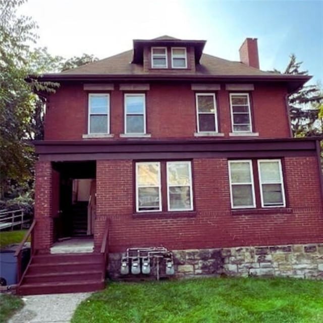 rear view of house featuring a chimney, a yard, and brick siding