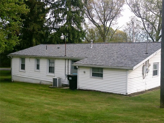 back of property featuring a shingled roof, a lawn, and central AC