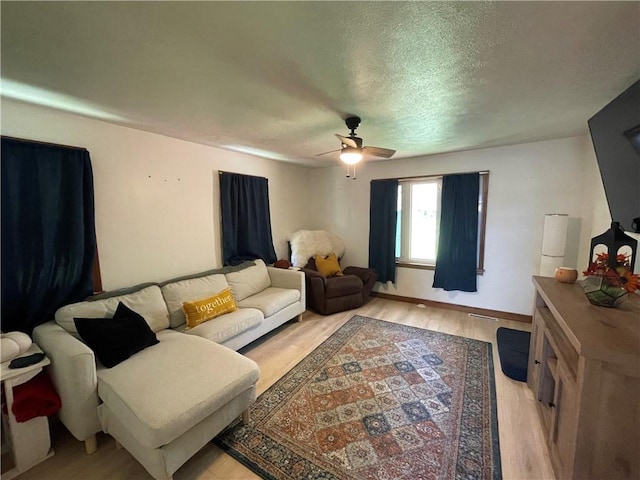 living room with ceiling fan, light wood-style flooring, a textured ceiling, and baseboards