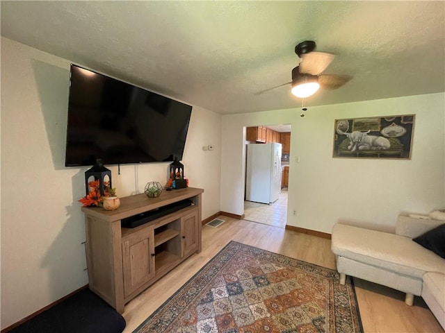 living area featuring light wood finished floors, a ceiling fan, and baseboards