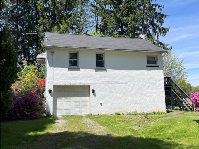 view of side of property with stucco siding, a garage, a lawn, and stairs
