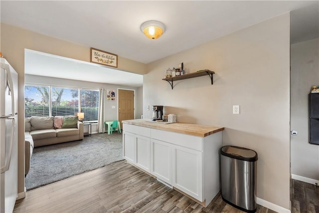 kitchen with butcher block countertops, light wood-type flooring, open shelves, white cabinets, and baseboards