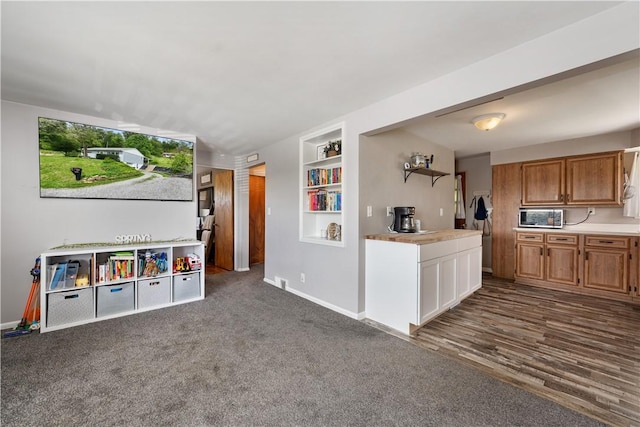 kitchen with stainless steel microwave, baseboards, built in shelves, and light countertops