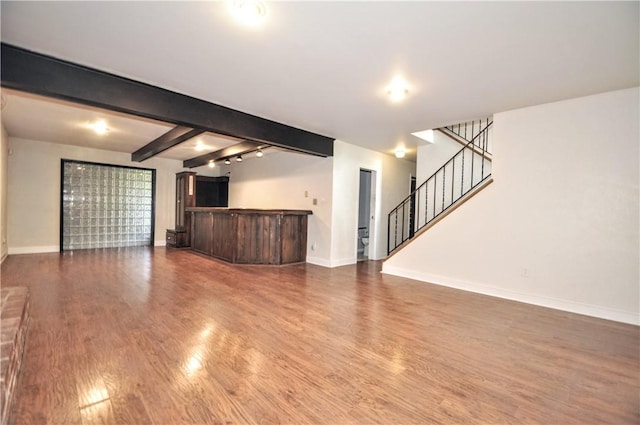 unfurnished living room with wood finished floors, stairway, baseboards, a dry bar, and beam ceiling