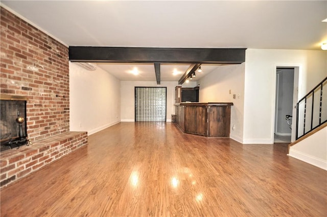 unfurnished living room featuring stairs, beam ceiling, baseboards, wood finished floors, and a dry bar