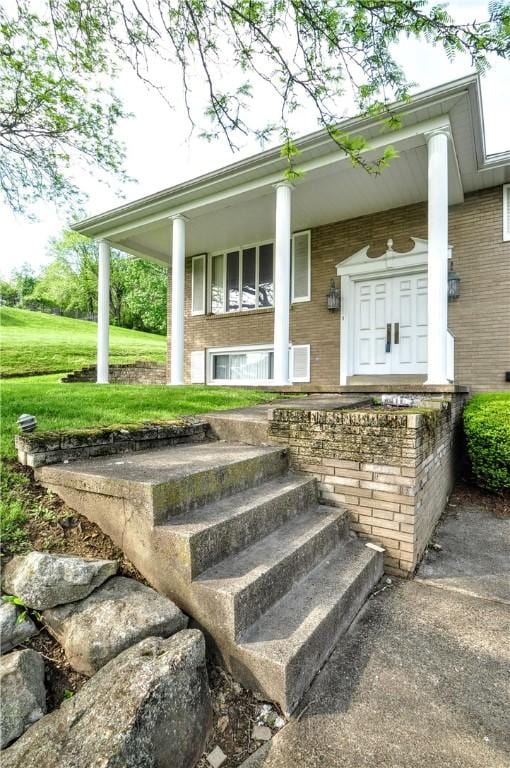 view of exterior entry featuring a porch, brick siding, and a yard