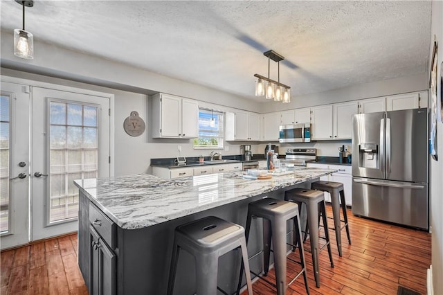 kitchen with appliances with stainless steel finishes, a sink, white cabinetry, hardwood / wood-style flooring, and a textured ceiling