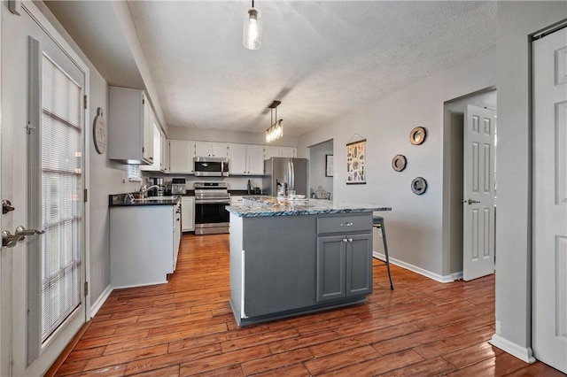 kitchen featuring stainless steel appliances, wood finished floors, baseboards, a center island, and white cabinets