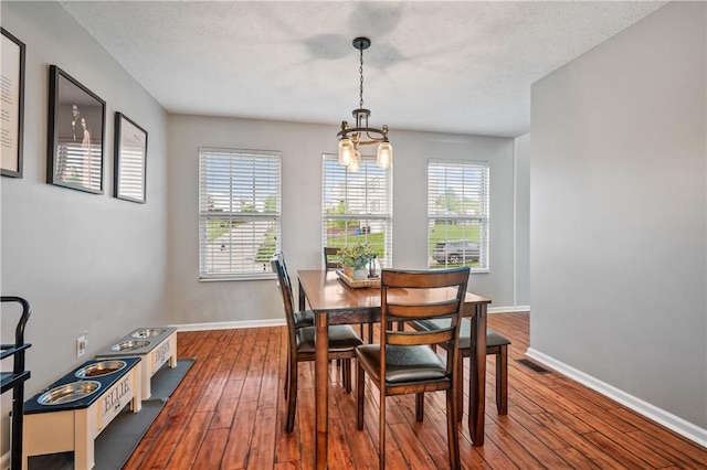 dining space with dark wood-style floors, a chandelier, baseboards, and a textured ceiling
