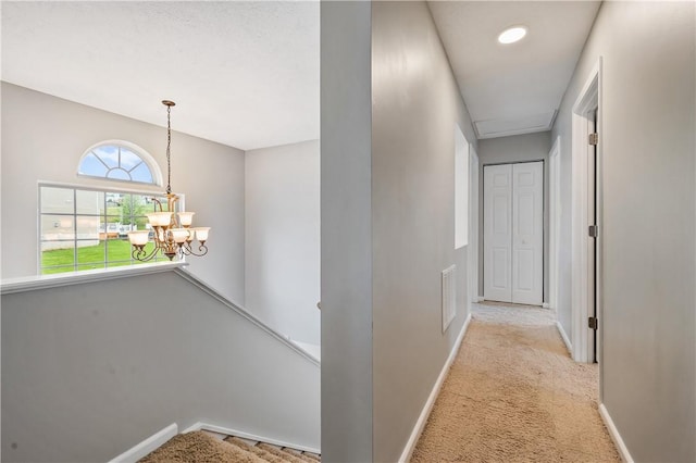hall featuring carpet flooring, a chandelier, baseboards, and an upstairs landing