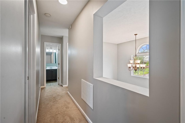 corridor with carpet floors, a chandelier, and baseboards