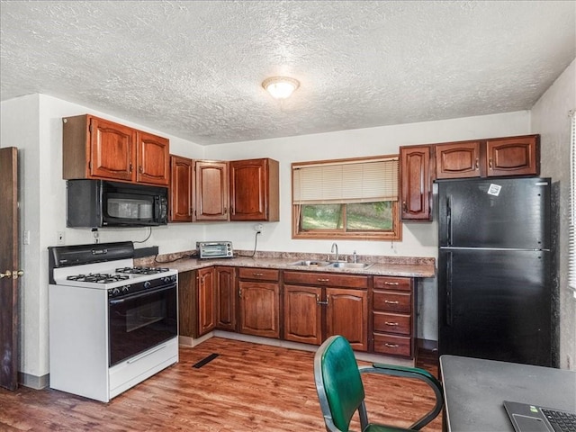 kitchen featuring black appliances, a sink, a textured ceiling, light wood-style floors, and light countertops