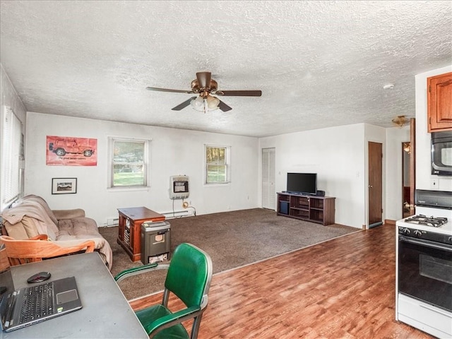living area with ceiling fan, a textured ceiling, wood finished floors, and a baseboard heating unit