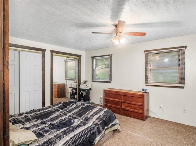 bedroom with a textured ceiling, carpet floors, two closets, and a ceiling fan