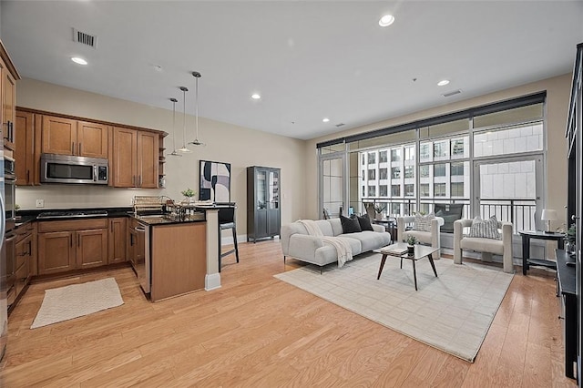 kitchen featuring appliances with stainless steel finishes, open floor plan, a peninsula, dark countertops, and brown cabinets