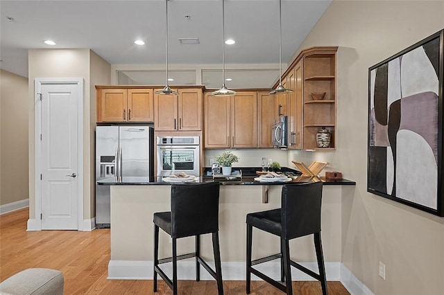 kitchen featuring appliances with stainless steel finishes, open shelves, dark countertops, a peninsula, and a breakfast bar
