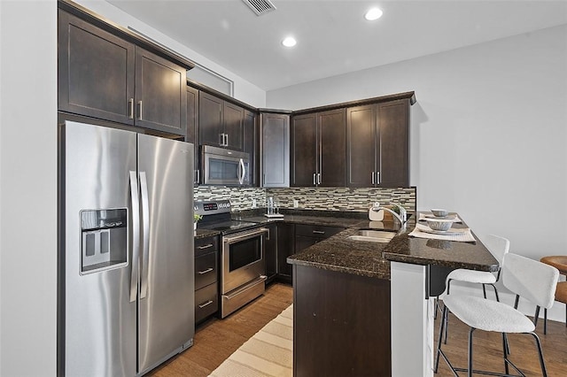 kitchen with stainless steel appliances, a sink, a peninsula, a kitchen bar, and dark brown cabinets