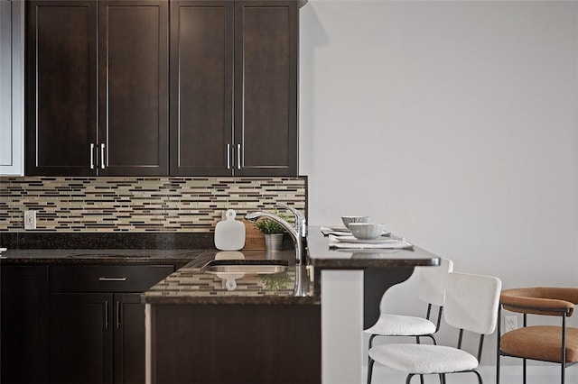 kitchen featuring a sink, dark brown cabinetry, tasteful backsplash, and a breakfast bar area