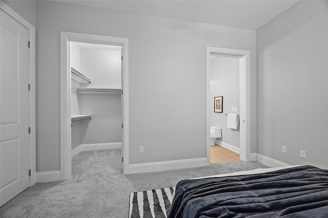 bedroom featuring carpet floors, baseboards, ensuite bathroom, and a walk in closet