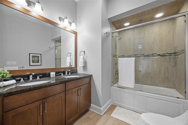 full bath featuring bath / shower combo with glass door, toilet, double vanity, and baseboards