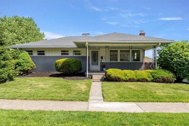 view of front facade featuring brick siding, a chimney, a front lawn, and covered porch