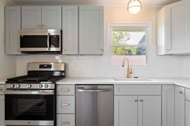 kitchen with appliances with stainless steel finishes, a sink, light countertops, decorative backsplash, and gray cabinets