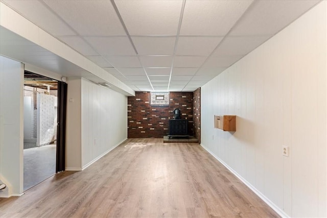 finished below grade area with a wood stove, wood finished floors, a drop ceiling, and baseboards