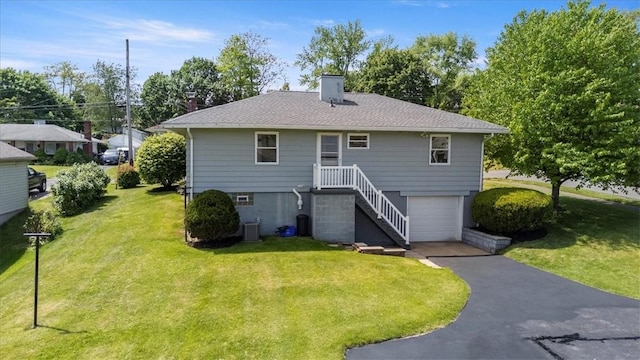 rear view of house featuring a chimney, a yard, an attached garage, asphalt driveway, and central AC