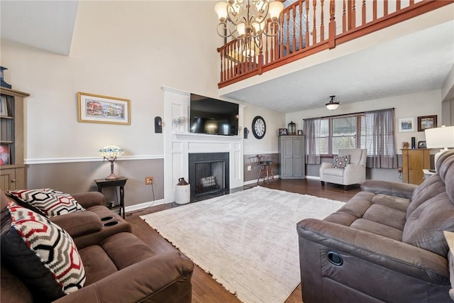 living area with dark wood-type flooring, a chandelier, a towering ceiling, a fireplace with flush hearth, and baseboards