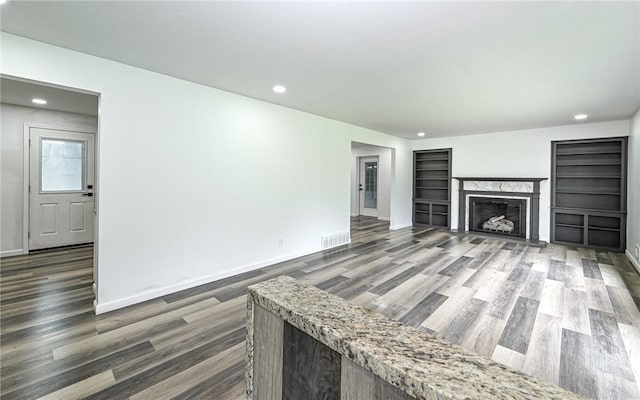 unfurnished living room with wood finished floors, recessed lighting, a premium fireplace, built in features, and baseboards