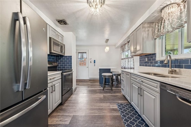 kitchen with appliances with stainless steel finishes, a sink, baseboards, decorative backsplash, and a chandelier