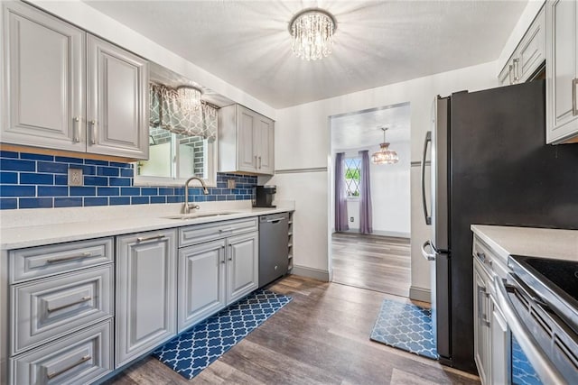 kitchen featuring a sink, a chandelier, dishwasher, decorative backsplash, and dark wood-style floors
