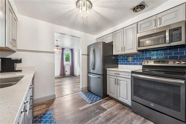 kitchen featuring appliances with stainless steel finishes, a chandelier, dark wood-type flooring, and decorative backsplash