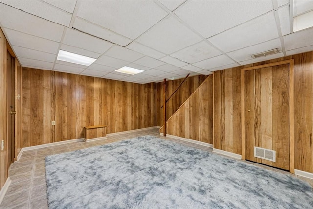 finished below grade area featuring wood walls, a paneled ceiling, and baseboards