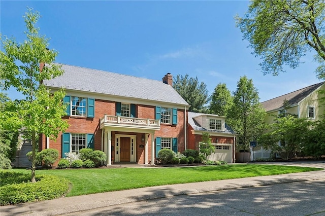 colonial inspired home featuring driveway, brick siding, a front yard, a chimney, and a balcony