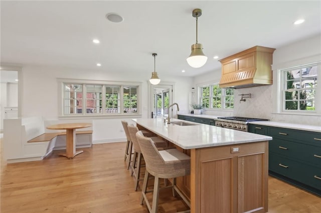 kitchen featuring a sink, light wood finished floors, recessed lighting, decorative backsplash, and a center island with sink