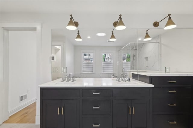 kitchen featuring a sink, light stone counters, dark cabinetry, decorative light fixtures, and light wood finished floors