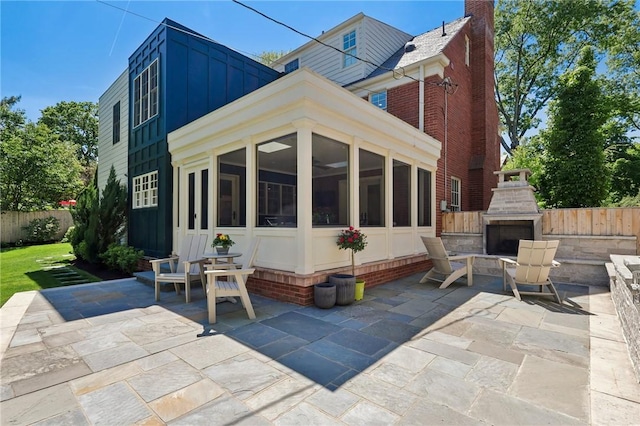 rear view of house featuring an outdoor fireplace, a patio area, a sunroom, and fence