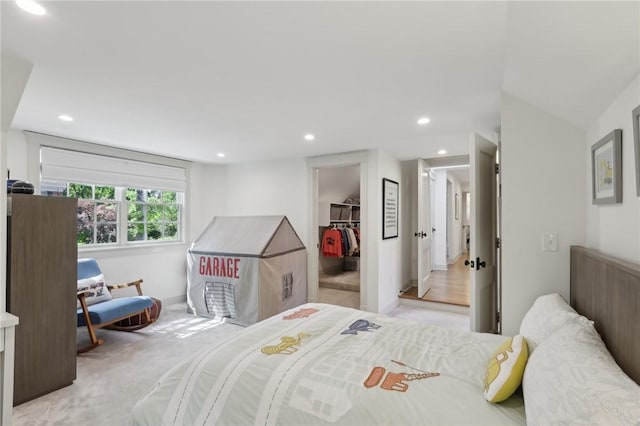 bedroom with a walk in closet, recessed lighting, light carpet, and a closet