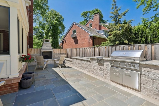 view of patio / terrace with exterior fireplace, a grill, an outdoor kitchen, and a fenced backyard