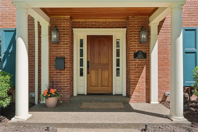 view of exterior entry with brick siding and a porch