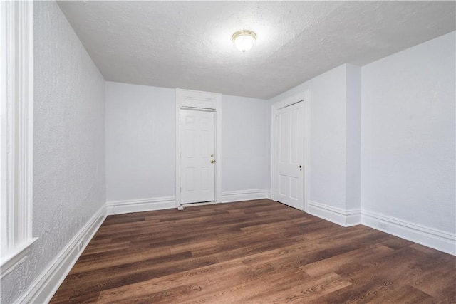 empty room featuring dark wood-type flooring, baseboards, a textured wall, and a textured ceiling