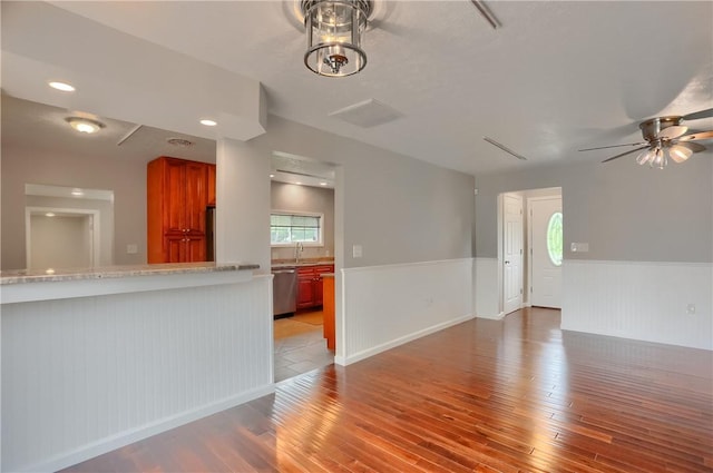 unfurnished living room with light wood-style floors, a wainscoted wall, a ceiling fan, and a sink