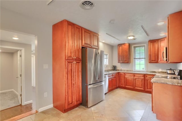 kitchen with stainless steel appliances, a sink, recessed lighting, brown cabinetry, and baseboards
