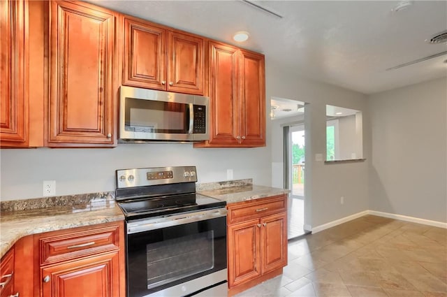 kitchen featuring stainless steel appliances, light tile patterned flooring, baseboards, and brown cabinets