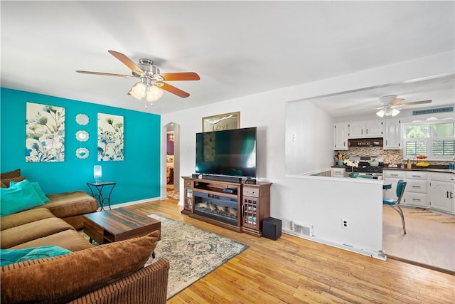 living area featuring a ceiling fan, light wood-style floors, and arched walkways